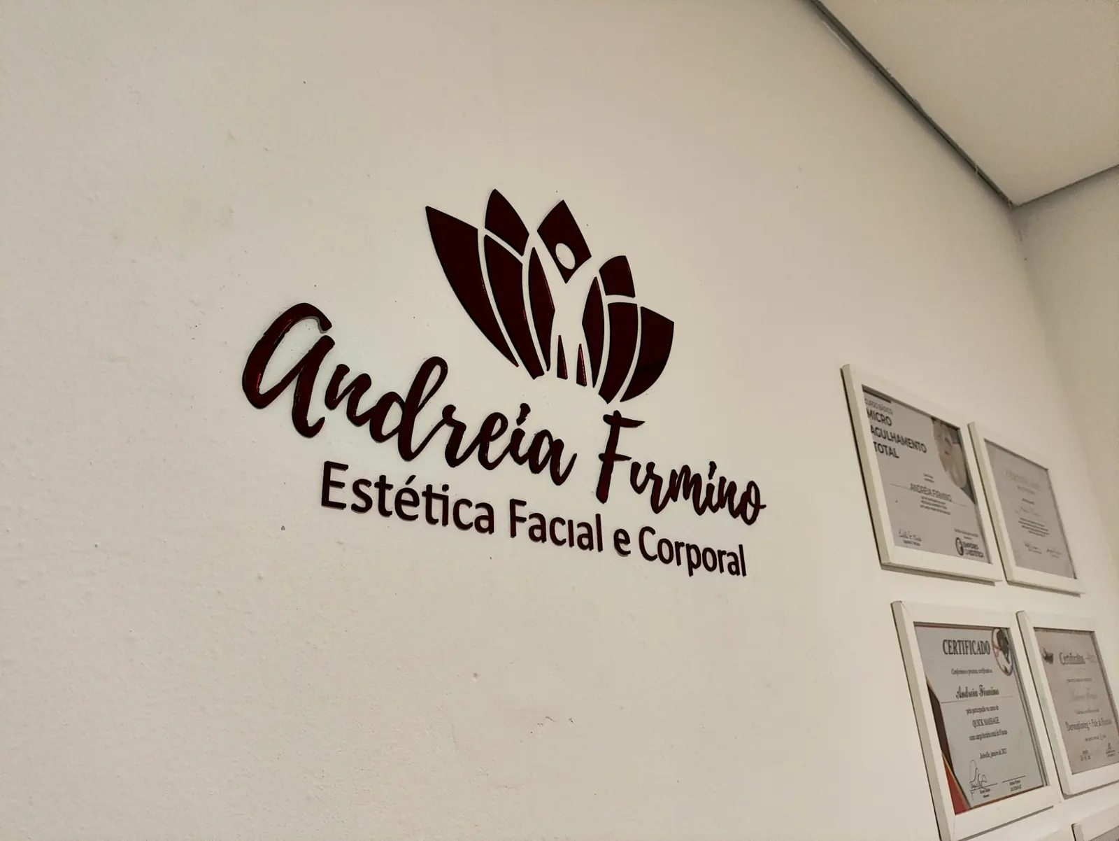 Parede com o letreiro Andreia Firmino Estética Facial e Corporal e certificados emoldurados